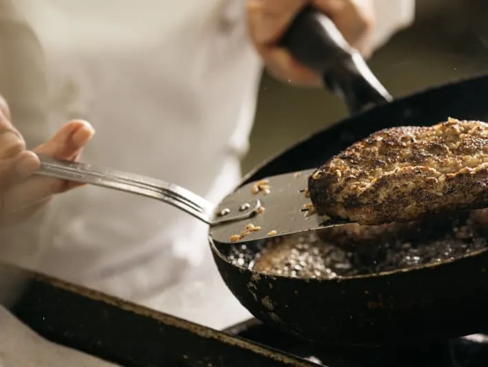 Flipping a hamburger patty in a frying pan with a spatula.