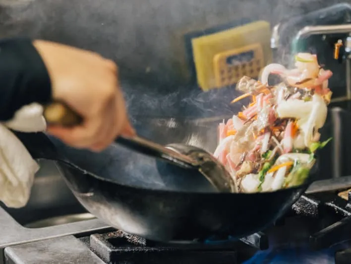 Stir-frying vegetables and meat in a wok on a gas stove.